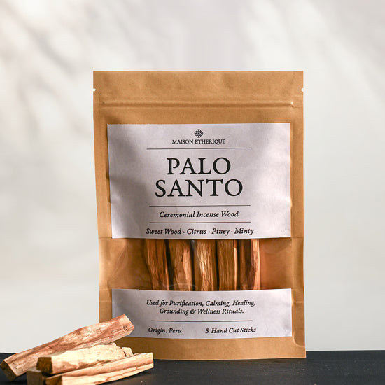 Kraft pouch of Maison Éthérique Palo Santo, five hand-cut sticks, on dark slate with loose sticks beside it.
