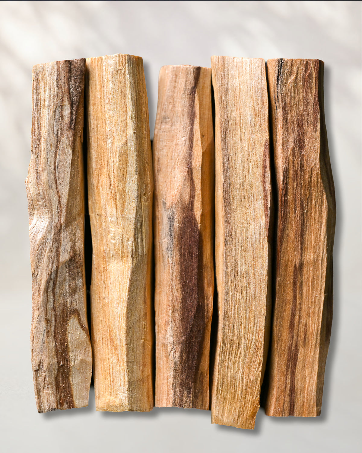 Five hand-cut Palo Santo sticks (Bursera graveolens) from Peru laid side by side on a pale background.