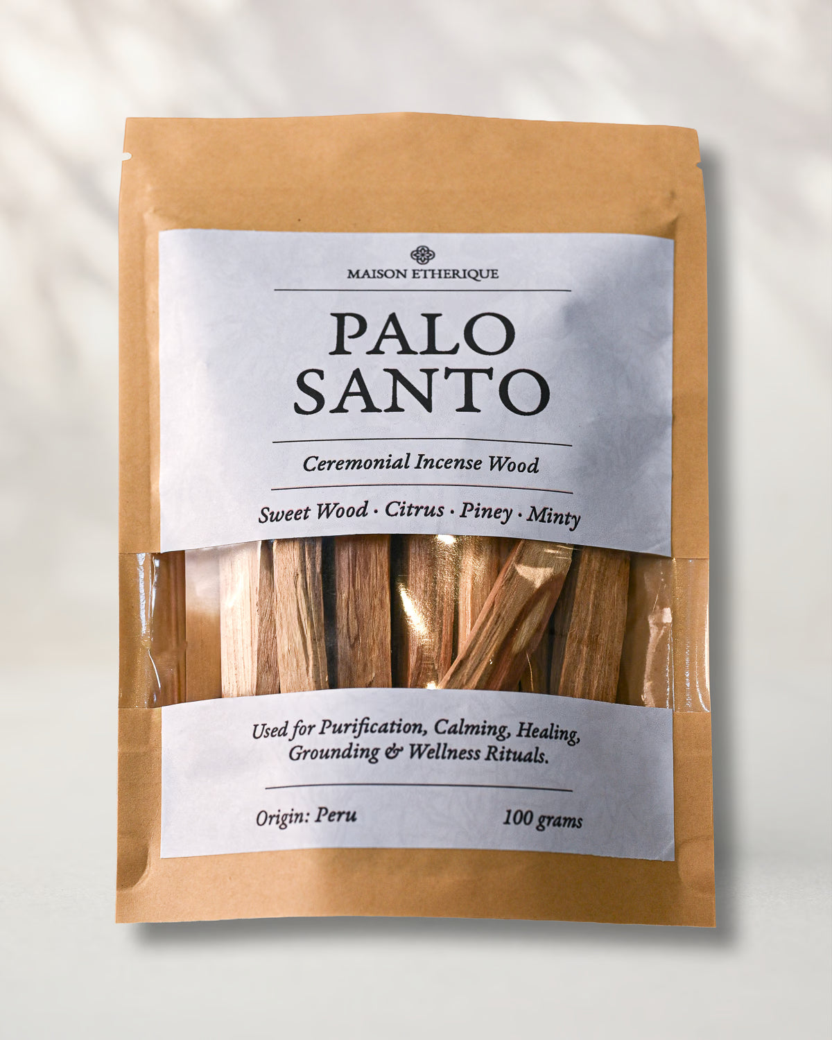 Front of a kraft pouch of Maison Éthérique Palo Santo, 100 g, sticks visible through a clear window, on a pale background.