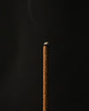 Close view of the tip of a Samten Tibetan incense stick with a wisp of smoke.
