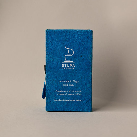 Back of a blue paper box of Stupa Sandalwood incense sticks, handmade in Nepal, on a pale background.