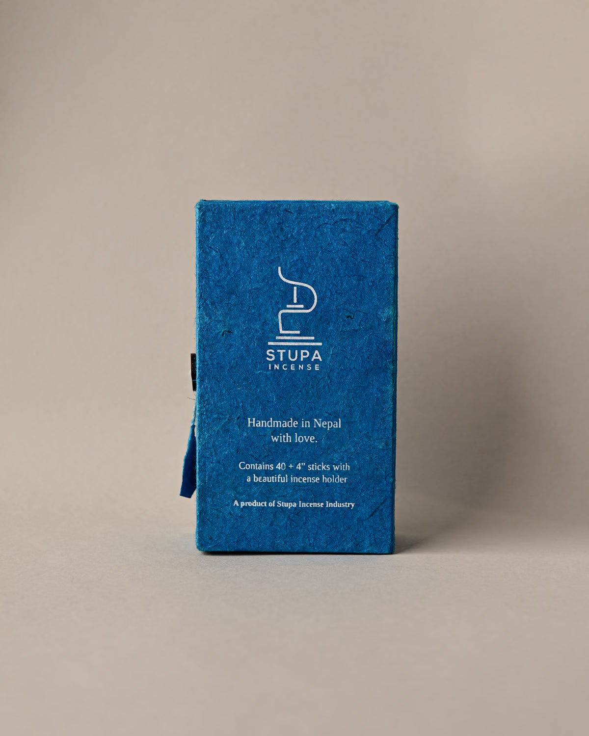 Back of a blue paper box of Stupa Sandalwood incense sticks, handmade in Nepal, on a pale background.
