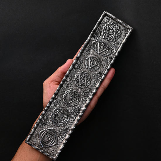 Hand holding the 7 Chakra metal incense stick holder against a dark background.