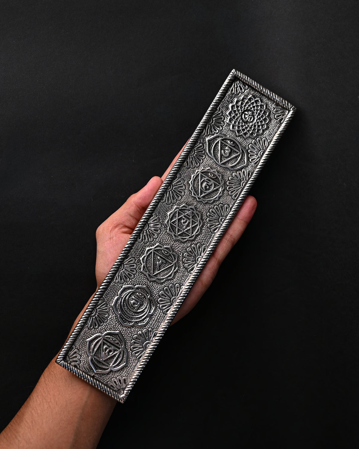 Hand holding the 7 Chakra metal incense stick holder against a dark background.