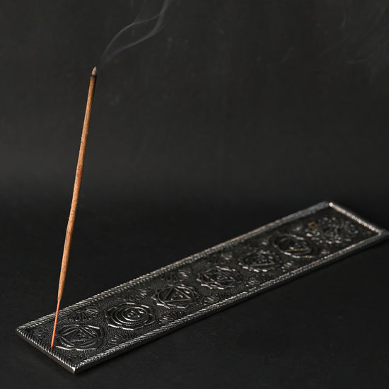 Incense stick burning at an angle in the 7 Chakra metal incense holder, a thin line of smoke rising.