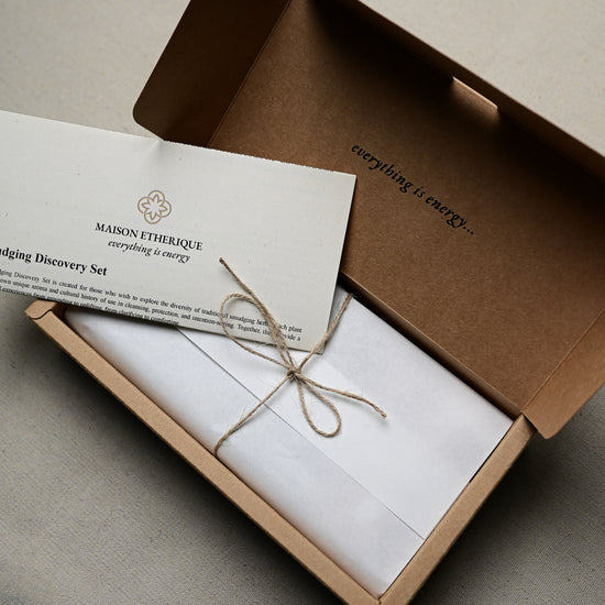 Open kraft box of the Maison Éthérique Smudging Discovery Set with a printed card tied in twine.