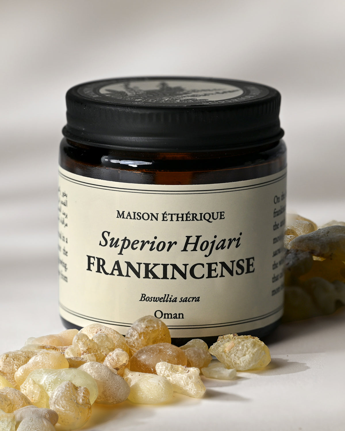 Amber glass jar of Maison Éthérique Superior Hojari Frankincense from Oman with pale frankincense tears in the foreground.