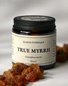 Amber glass jar of Maison Éthérique True Myrrh from Yemen with amber-red myrrh resin pieces in the foreground.