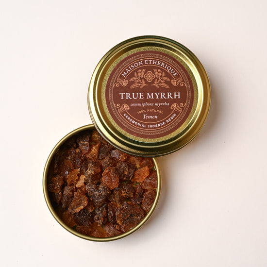 Open gold tin of Maison Éthérique True Myrrh (Commiphora myrrha) from Yemen, amber-red resin pieces visible inside.