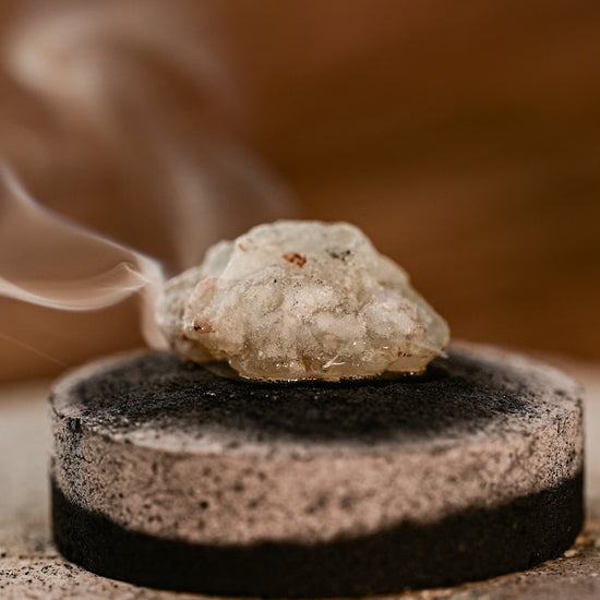 Piece of White Copal resin smouldering on a charcoal disc, smoke rising.