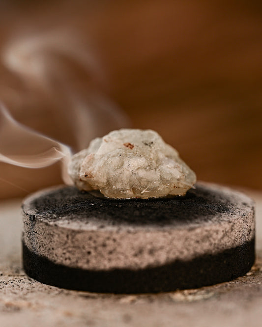 Piece of White Copal resin smouldering on a charcoal disc, smoke rising.
