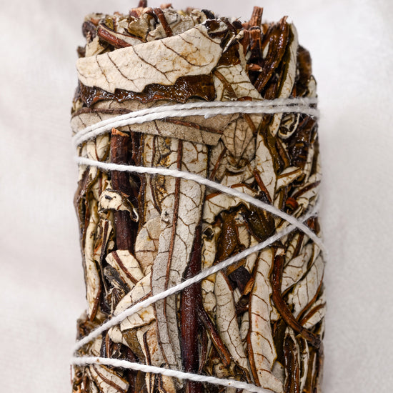 Yerba santa smudge stick, dried leaves and dark stems bound with white string, shown close against a pale background.