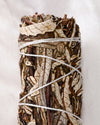 Yerba santa smudge stick, dried leaves and dark stems bound with white string, shown close against a pale background.