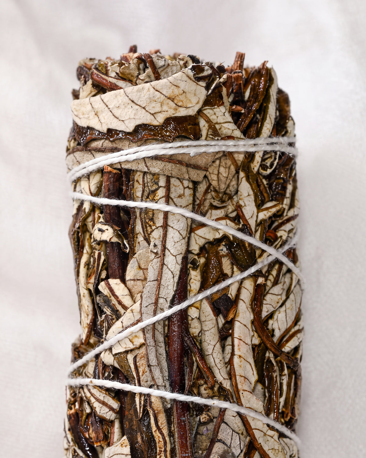 Yerba santa smudge stick, dried leaves and dark stems bound with white string, shown close against a pale background.