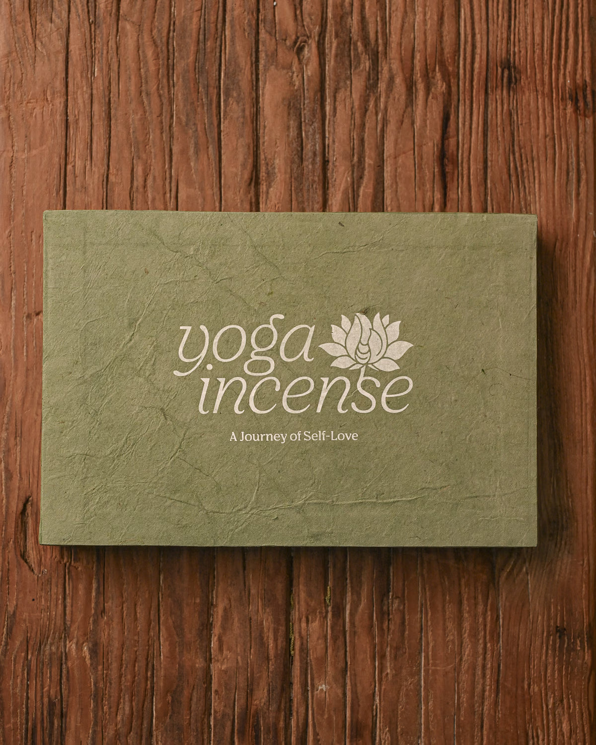 Closed Yoga Incense gift box in green handmade paper on a wooden surface.