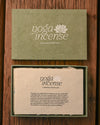 Yoga Incense gift box in green handmade paper, the lid above and the open box with its printed insert below, on a wooden surface.