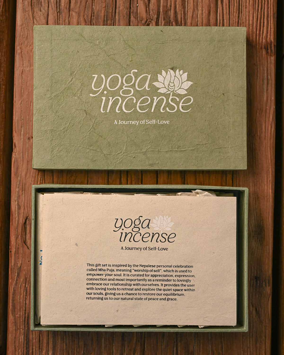 Yoga Incense gift box in green handmade paper, the lid above and the open box with its printed insert below, on a wooden surface.
